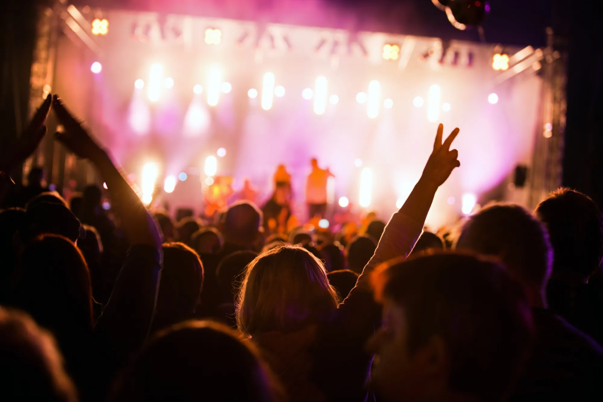 Fans with their hands raised in front of a lit festival stage